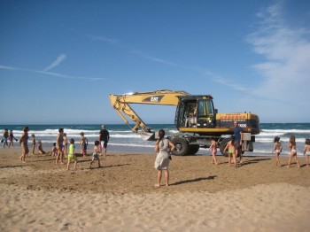 Xiquets jugant a la platja amb una excavadora al costat Xiquets jugant a la platja amb una excavadora al costat